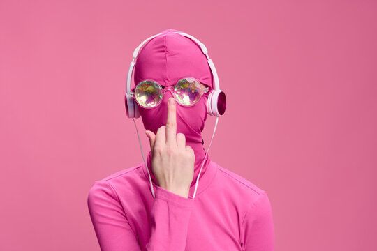 Conceptual creative art photo of a man in Total Pink on a pink background wearing a mask and glasses, who is adjusting his glasses with the middle finger of his hand