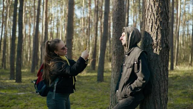 girl takes a picture of a guy on the phone in the forest