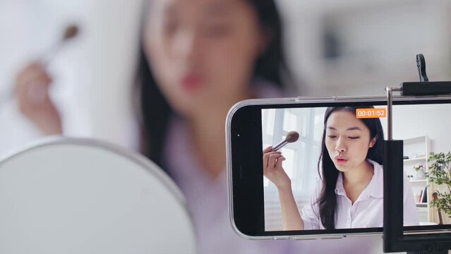 Young Asian woman blogger recording make-up tutorial on smartphone camera
