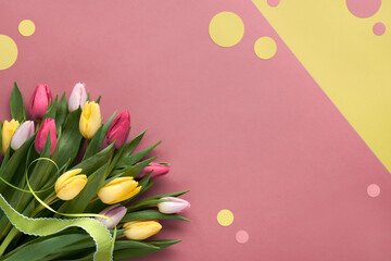 Bunch of red and yellow tulips with ribbon. Corner composition, flat lay on layered pink and yellow paper. Decorative paper circles, copy-space, place for text.