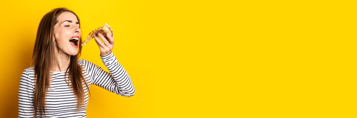 young woman with closed eyes eating a slice of hot fresh pizza on a yellow background. Banner