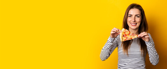 smiling young woman holding a slice of hot fresh pizza on a yellow background. Banner