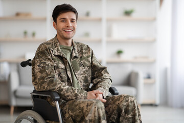 Happy young man soldier sitting in wheelchair, home interior
