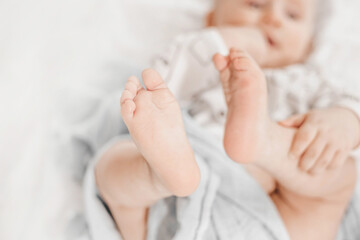 the child lies on the bed in blankets with his legs up. copy space. Development of leg motor skills in a child
