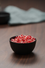pomegranate seeds in a black bowl on walnut table