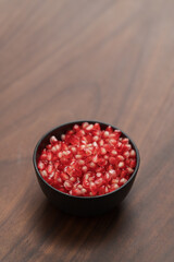 pomegranate seeds in a black bowl on walnut table