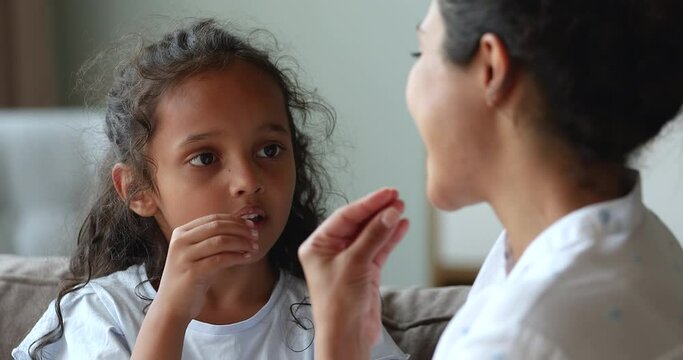 Focused preschool Indian girl little patient of speech therapist surdologist learning to spell sounds correctly imitate teacher doctor. Small child work on pronunciation do phonetic exercises with mom