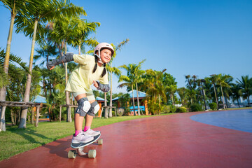 asian child or kid girl smile playing surf skate or skateboard in skatepark and extreme sports exercise to wearing helmet elbow pads wrist and knee support for body safety protect at bang phra park © kornnphoto