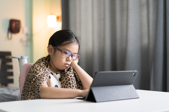 Asian child unhappy bored video call learning and study online class on computer tablet or kid girl student wearing blue block eyeglasses for eye protection or person stressed learn from home school