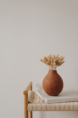 Aesthetic luxury bohemian flowers composition. Elegant gentle rabbit tail grass stalks bouquet in ginger clay pot on rattan bench - obrazy, fototapety, plakaty