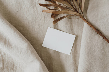 Flatlay of blank paper card, dried protea flower on neutral beige crumpled linen cloth. Business...