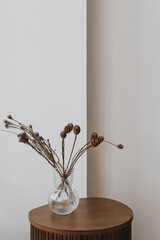 Dried pampas grass and flowers bouquet in glass vase on wooden side table against white wall....