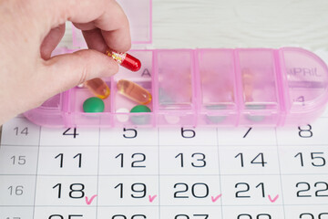 Womans hand puts a capsule in a pink plastic pill organizer. Planning of taking prescribed...