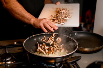 male hand pours chopped champignons from cutting boards into a frying pan