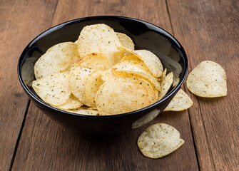 Crispy potato chips in black bowl on old wooden table background. vintage styles
