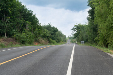 Long straight asphalt road ahead. With trees forest two beside. Trees were densely growing on both sides. White line and the solid yellow line in the no-overtaking zone. Cross-provincial area.