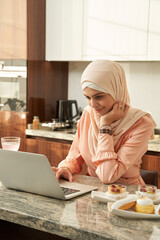 Smiling Muslim woman using laptop at home