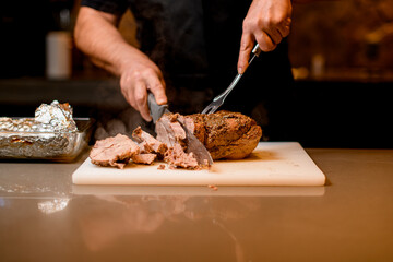 man chef accurate cuts cooked fried meat on white cutting board.