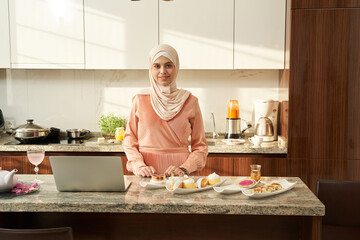 Muslim woman cooking and using laptop at home