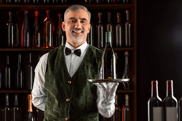 Sommelier wine steward with a bottle of wine. Examination of wine products. Restaurant waiter among shelves of wine bottles. Stylish middle-aged man with a grey beard