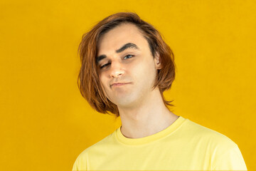 Young man with long hair. Portrait of skeptic, unbeliever, sceptic, non-believer guy on a yellow background