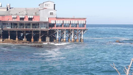 Waterfront beachfront cafe on piles, pillars or pylons, Monterey beach, California coast aesthetic, USA. Sea ocean water waves and building architecture. Summer tourist vacations in watersibe resort.