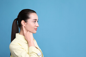 Young woman pointing at her ear on light blue background. Space for text - obrazy, fototapety, plakaty