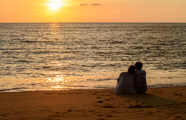 A couple sits on the beach watching the sunset at Khao Lak