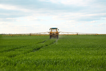 Fototapeta premium Tractor spraying pesticide in field on spring day. Agricultural industry