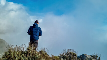 Man with panoramic view from Monte Comune on thick white clouds and blue sky near coastal town...