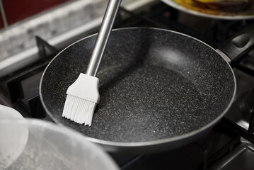 Greasing frying pan on stove in kitchen, closeup