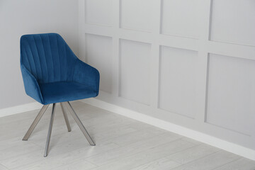 Stylish blue armchair near light wall in room. Space for text