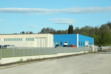 Factory building with parking lot surrounded by fence on sunny day