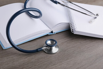 Book, stethoscope and notebook on wooden table. Medical education