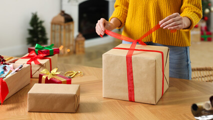 Woman wrapping Christmas gift at wooden table indoors, closeup - obrazy, fototapety, plakaty