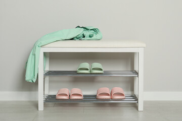 Stylish storage bench with different pairs of rubber slippers near white wall in hall