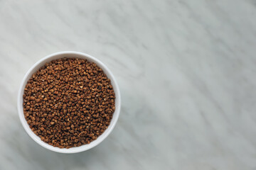 Bowl with uncooked buckwheat porridge on white marble table, top view. Space for text
