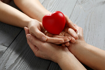 Young and elderly women holding red heart at grey wooden table, closeup
