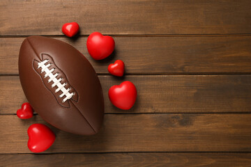 American football ball and hearts on wooden background, flat lay. Space for text