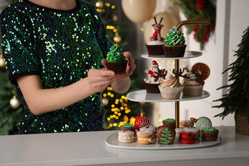 Woman with Christmas tree shaped cupcake near white table indoors, closeup