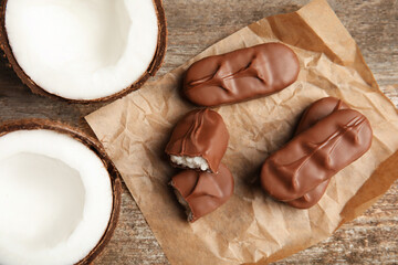 Delicious milk chocolate candy bars with coconut filling on wooden table, flat lay