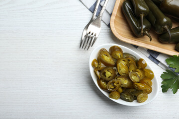 Bowl with slices of pickled green jalapeno peppers on white wooden table, flat lay. Space for text