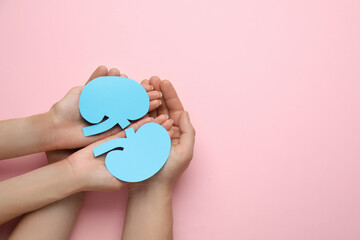 People holding paper cutout of kidneys on pink background, top view. Space for text
