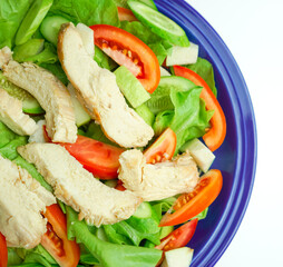 Salad with difference lettuce cucumber tomatoes and baked chicken breast in blue dish on isolates white background
