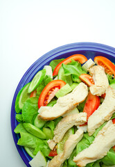 Salad with difference lettuce cucumber tomatoes and baked chicken breast in blue dish on isolates white background