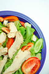 Salad with difference lettuce tomato and baked chicken breast on blue dish