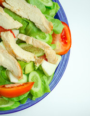 Salad with difference lettuce tomato and baked chicken breast on blue dish