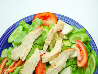 Salad with difference lettuce tomato and baked chicken breast on blue dish