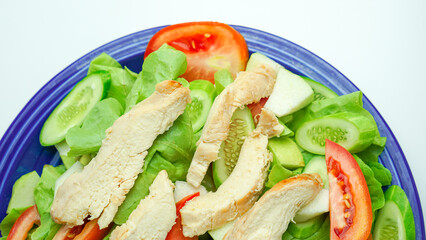 Salad with difference lettuce tomato and baked chicken breast on blue dish