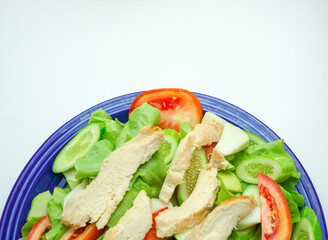 Salad with difference lettuce tomato and baked chicken breast on blue dish